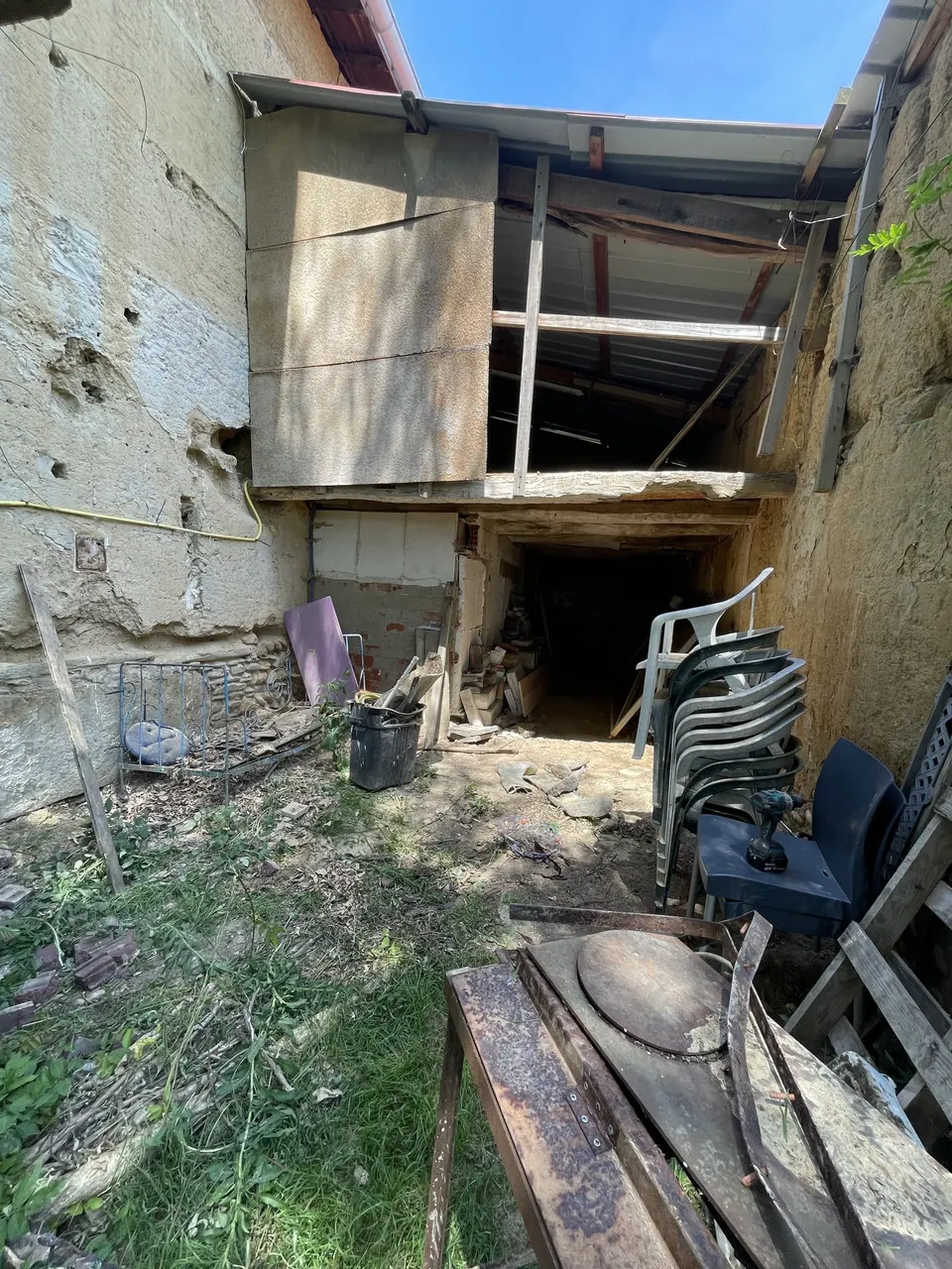 Autre vue de la cour avant travaux, herbe, planches et chaises empilées.