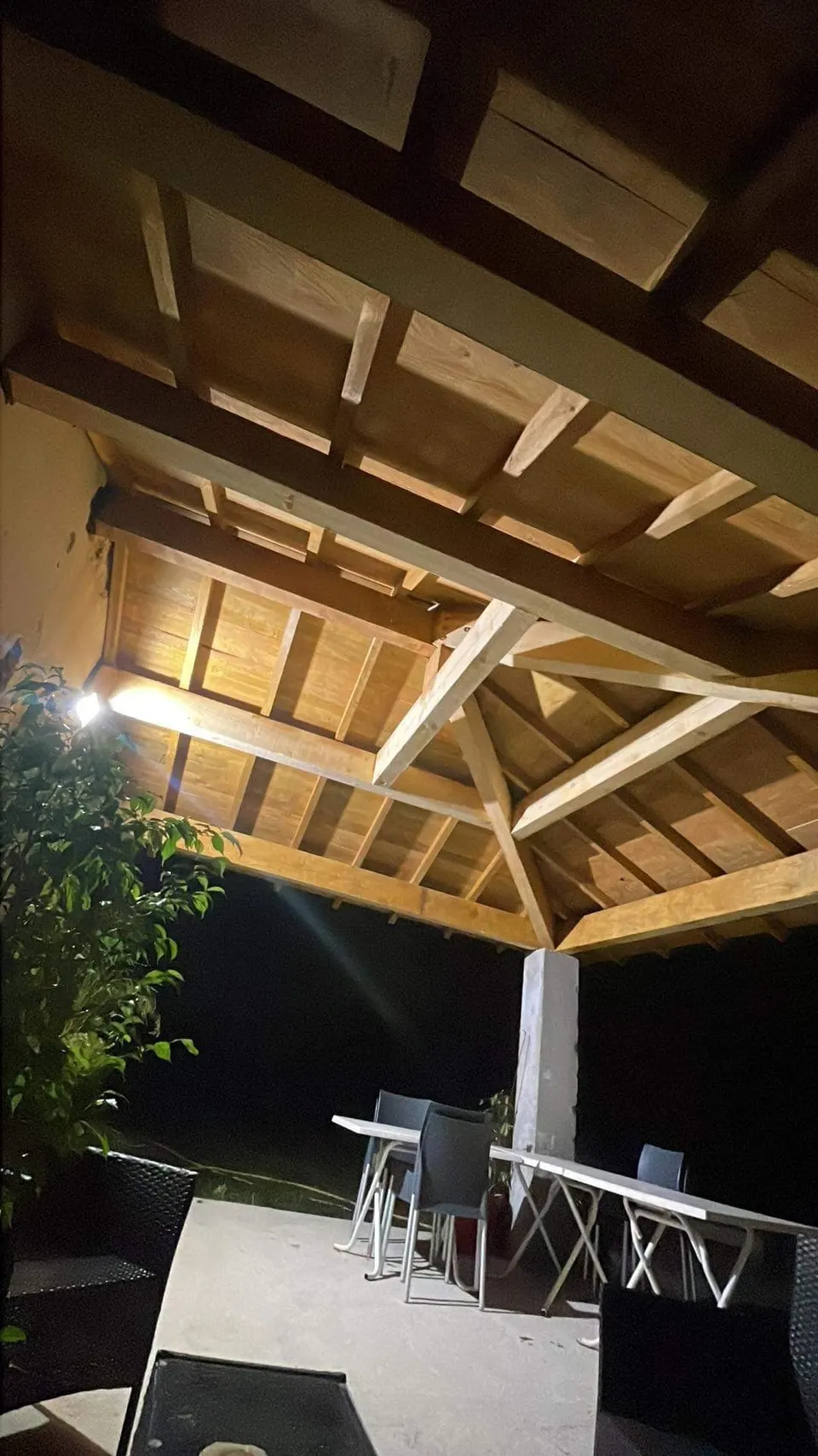 Vue sous la toiture : chevrons et voligeage en bois, éclairés de nuit.