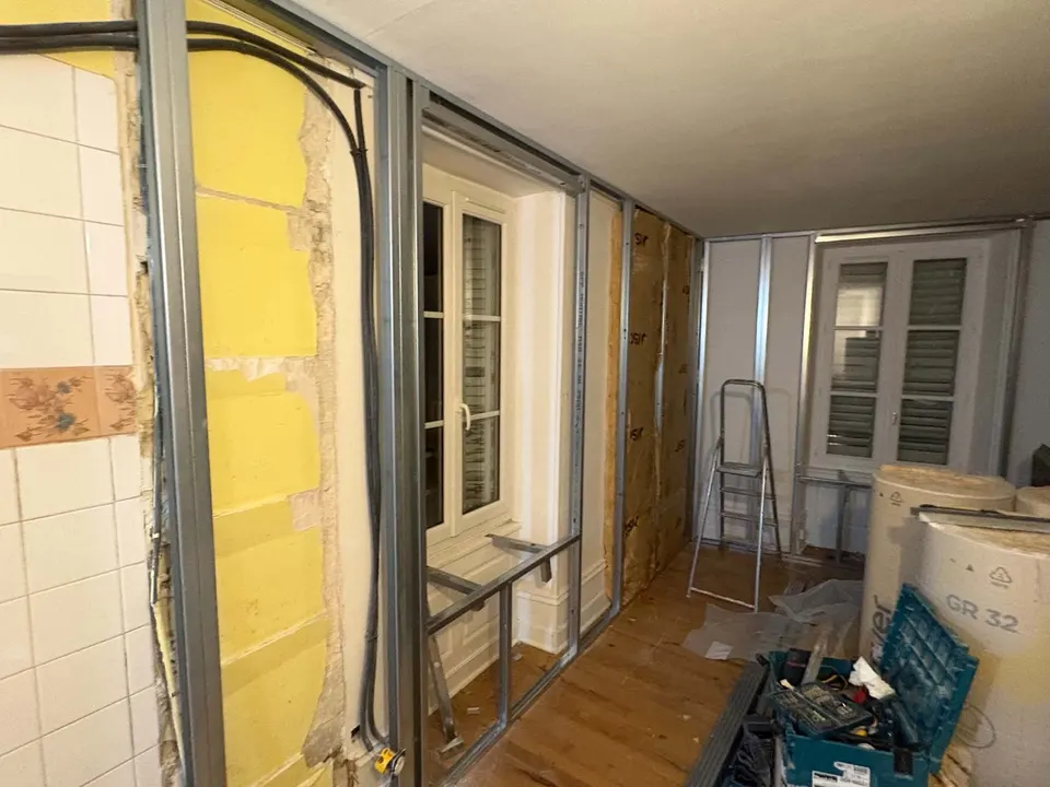 Ossature et isolant jaune en place le long de la fenêtre, face à l'ancien carrelage.