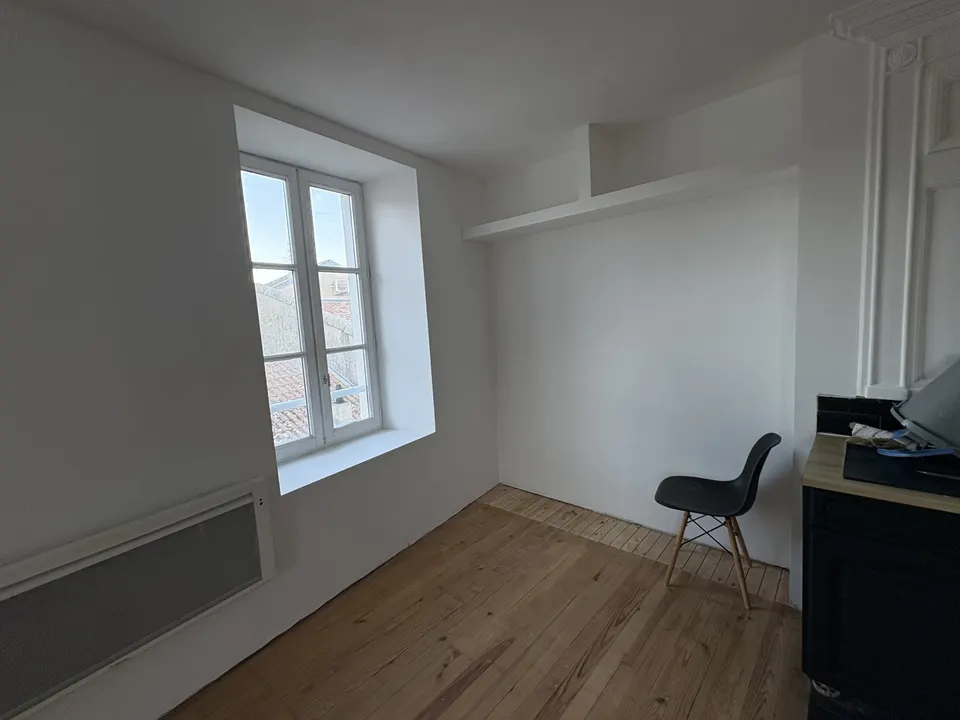 Après les travaux : pièce peinte en blanc, parquet apparent et fenêtre claire.
