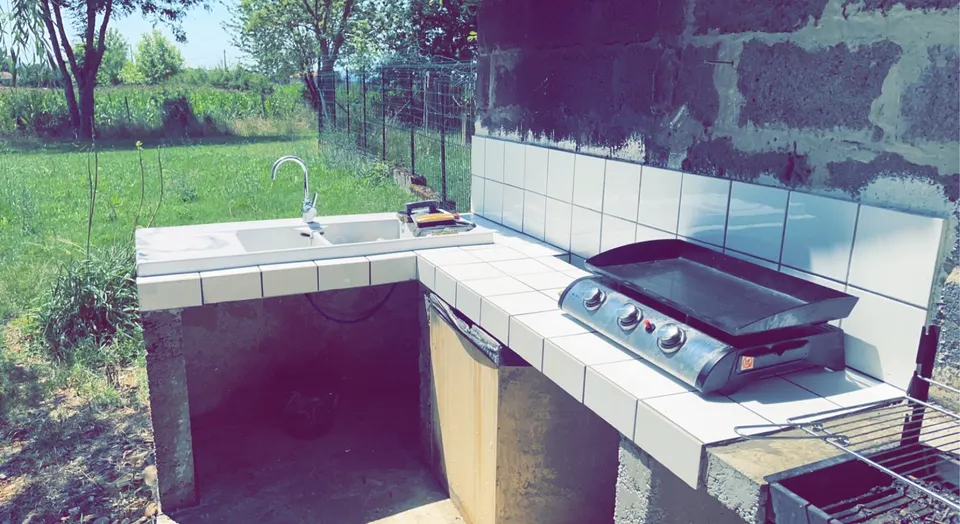 Plan de travail carrelé avec évier, plancha à gaz et crédence blanche en extérieur.