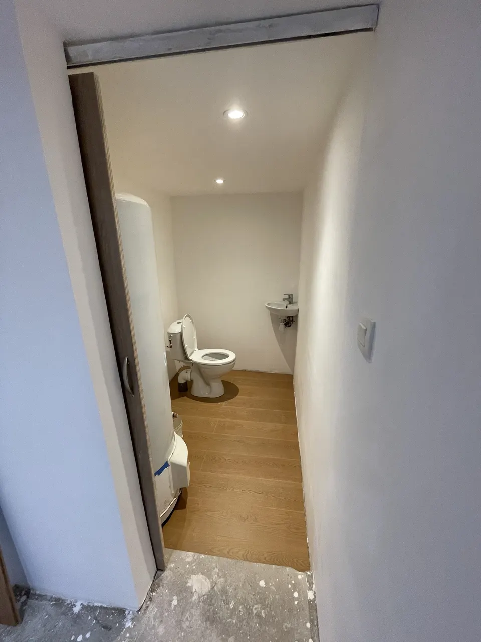 Toilettes terminées : cuvette, lave-mains, parquet stratifié et spots encastrés