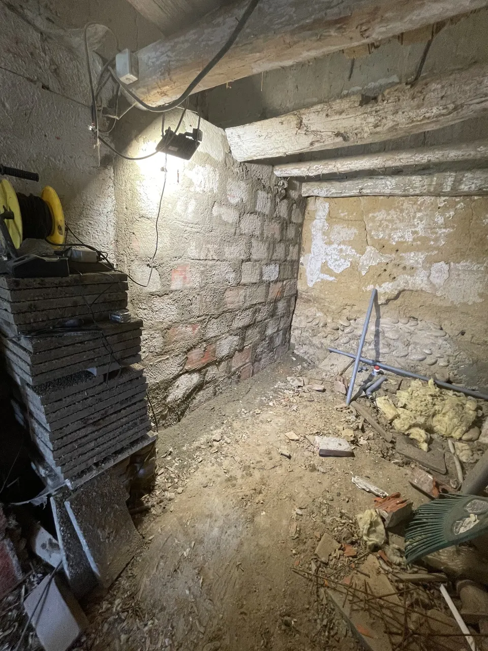 Fond de la cave encombré : murs en pierre, câbles et gravats