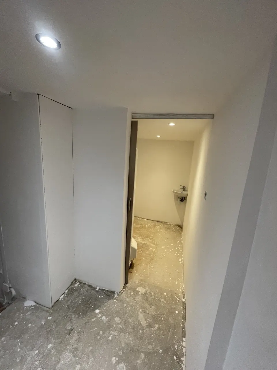 Couloir plâtré avec porte coulissante entrouverte sur les toilettes