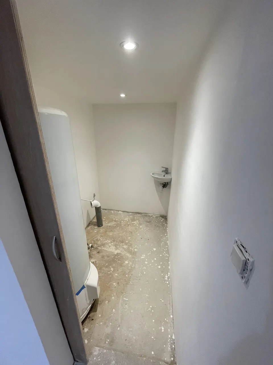 Toilettes avant la pose du sol : lave-mains installé, murs peints, dalle brute