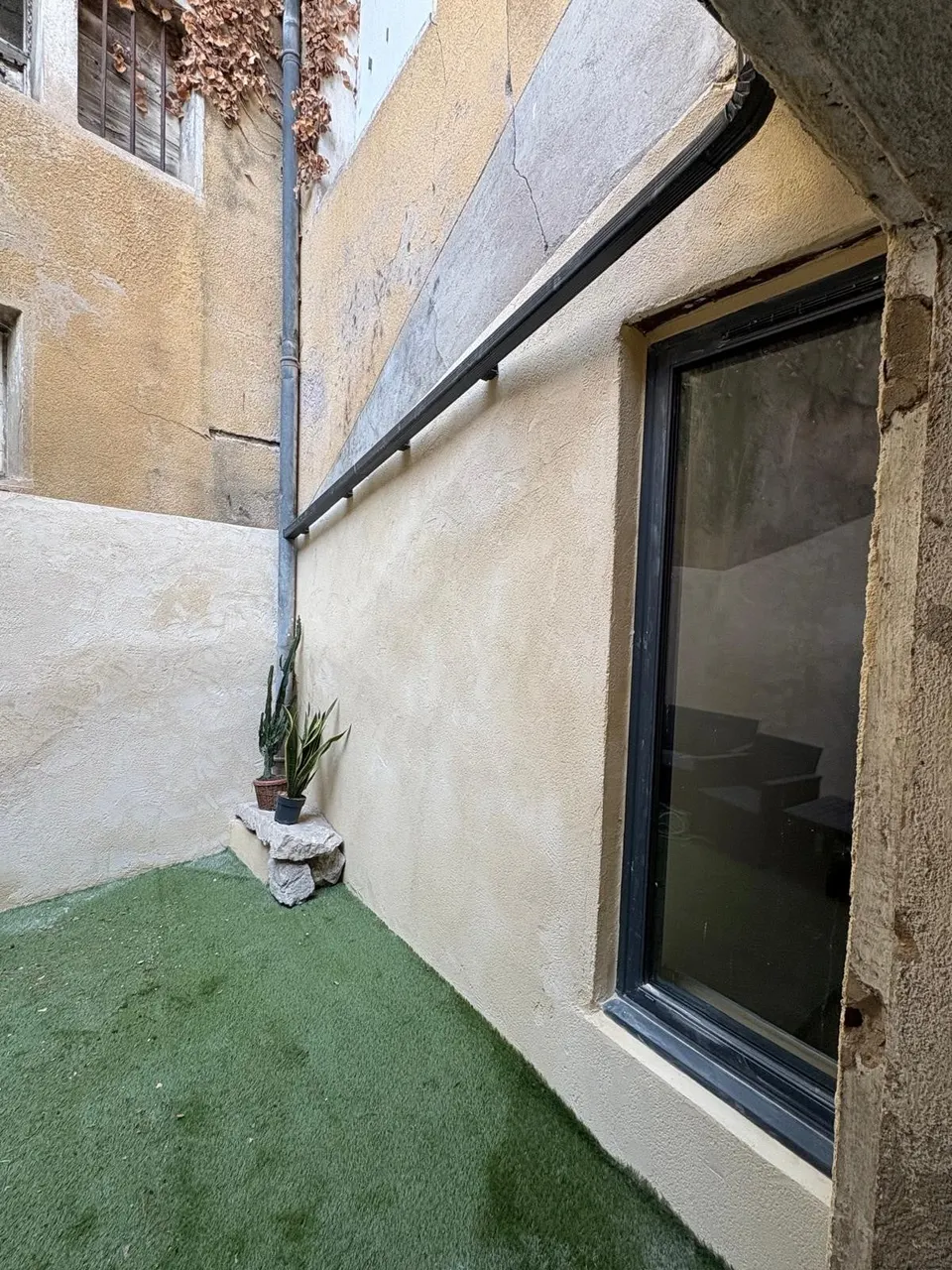 Murs crépis, baie vitrée noire et gazon synthétique posé au pied de la façade.