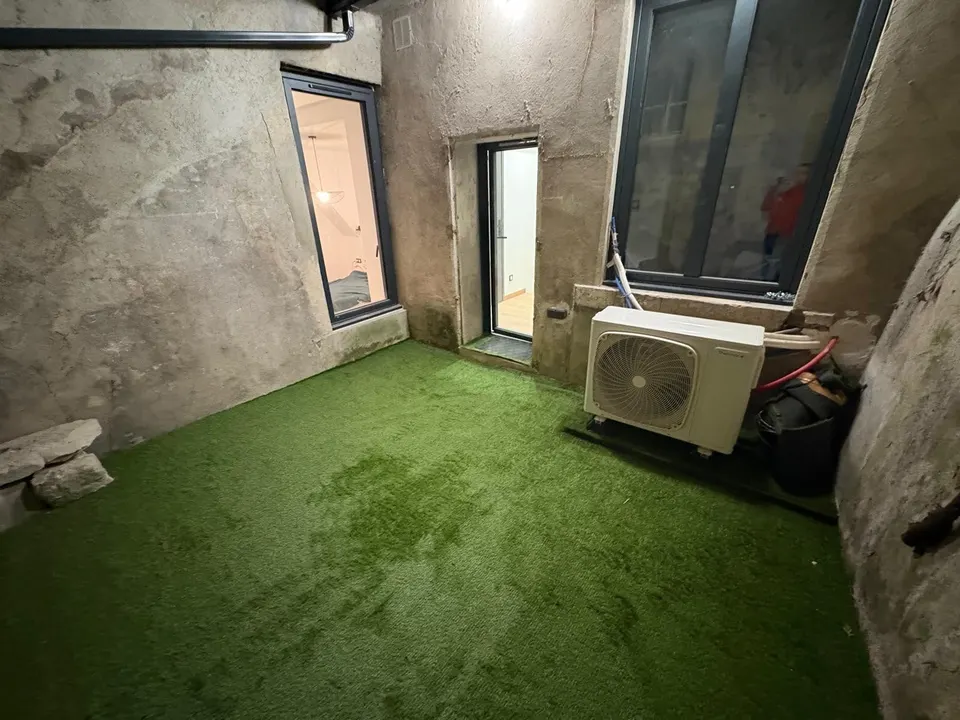Vue de la cour avec le gazon posé, la porte vitrée et la pompe à chaleur.