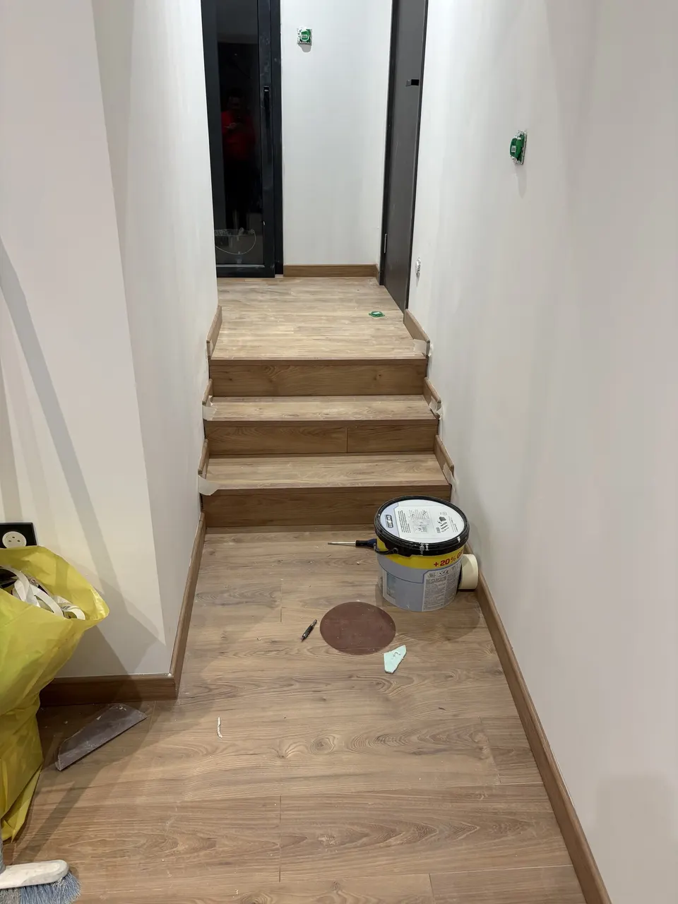Couloir et marches parquetés, avec les outils et le seau de chantier.