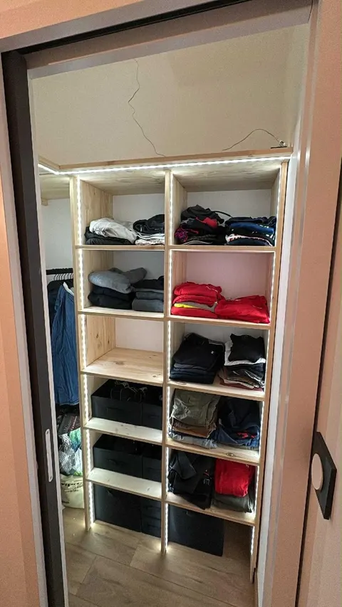 Dressing en bois brut éclairé par un bandeau LED, avec bacs de rangement en bas.