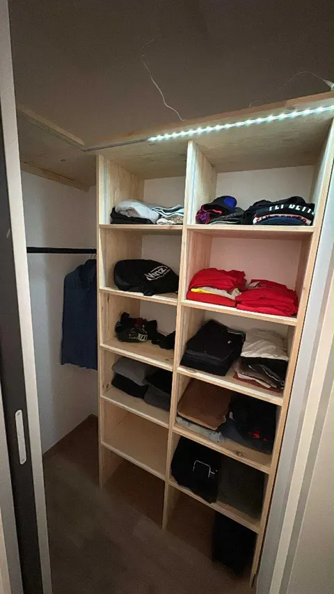 Casiers en bois remplis de vêtements pliés, tringle à cintres sur le côté.