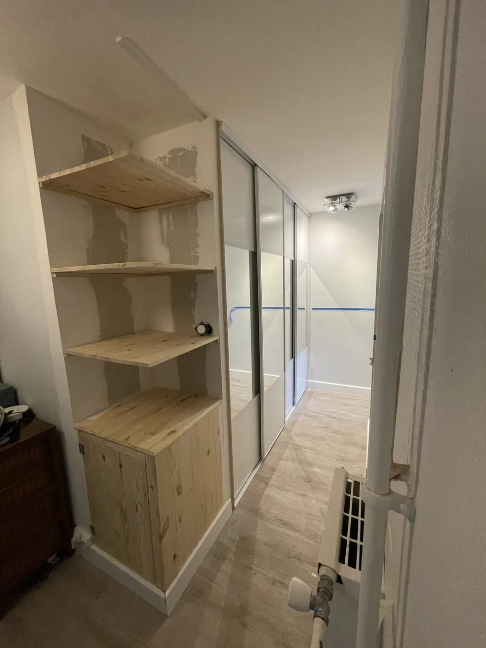 Étagères en bois brut et meuble bas à côté des portes coulissantes déjà posées.