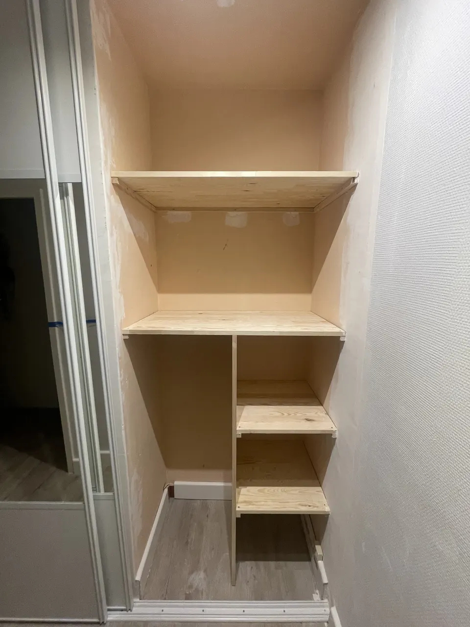 Niche équipée d'étagères hautes et de tablettes à côté des portes coulissantes.
