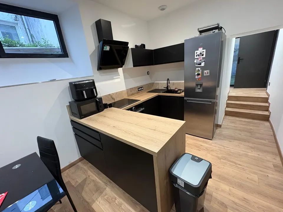 Cuisine terminée : meubles noirs, plan de travail en bois, four et hotte en place.