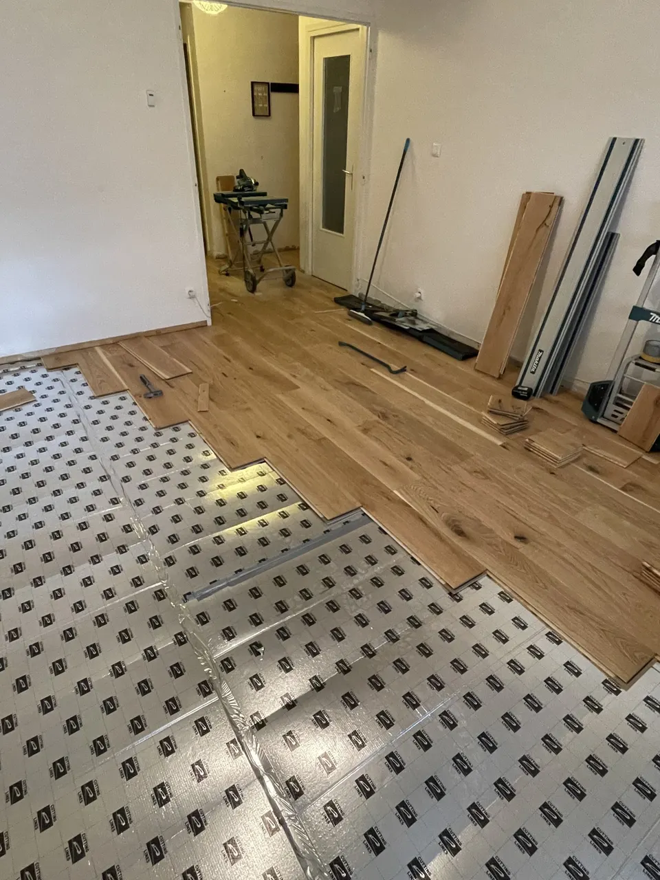 Détail de la pose : lames de chêne sur la sous-couche, outils de coupe au fond