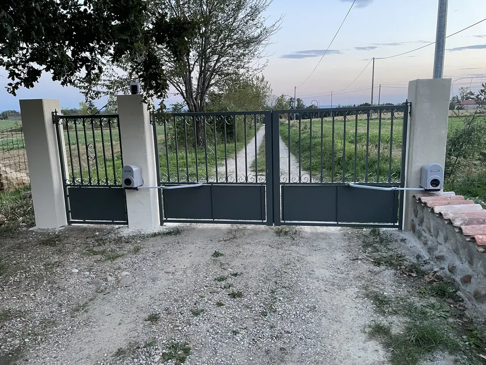 Portail battant motorisé gris anthracite entre deux piliers, muret de pierre à droite