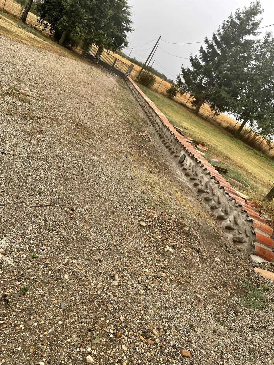 Muret de galets surmonté de tuiles le long de l'allée de gravier