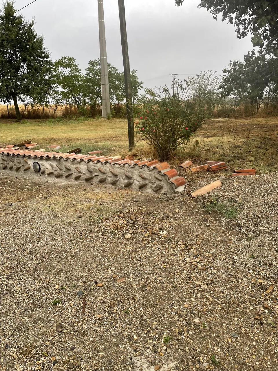 Muret de pierre et tuiles vu depuis l'allée de gravier