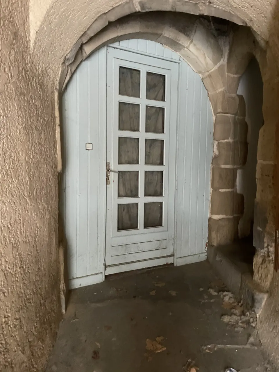 L'ancienne porte bleue vitrée avant travaux, sous l'arc en pierre.