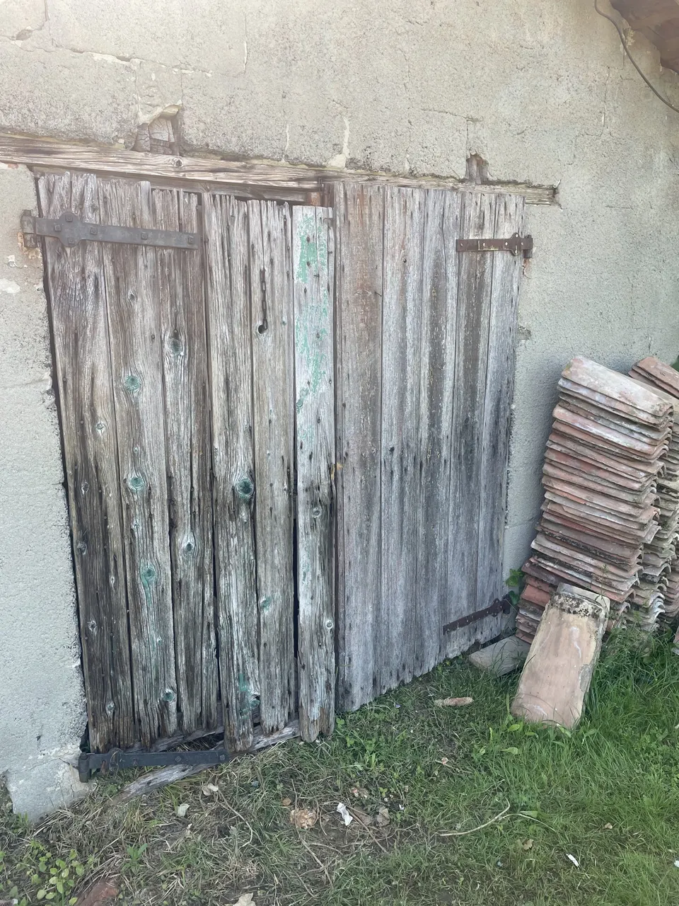 Porte de grange en bois grisé et très abîmé, pile de tuiles à droite