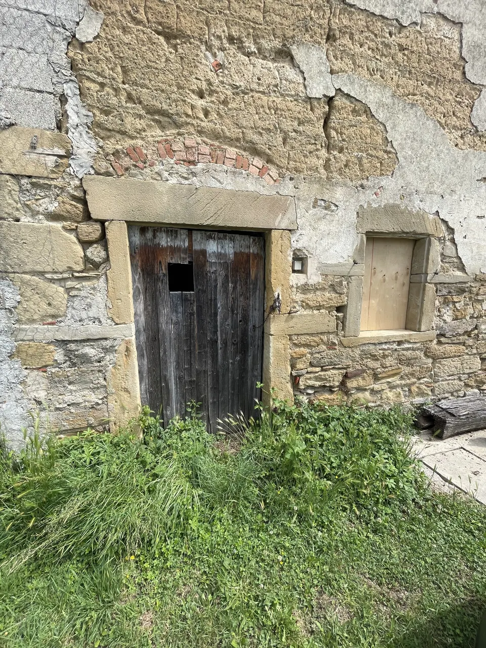 Petite porte en bois noirci dans un encadrement de pierre, fenêtre bouchée