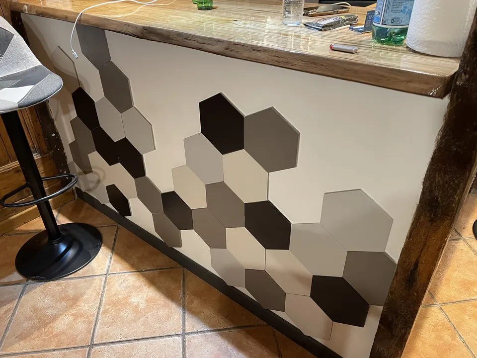 Façade du bar habillée de carrelage hexagonal, sous un plateau en bois.