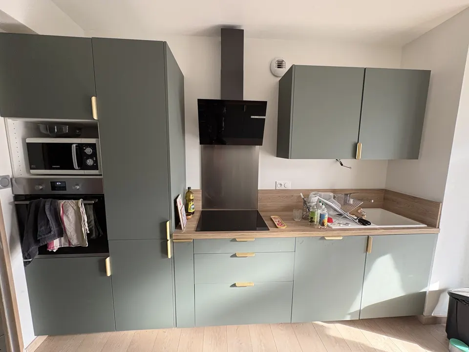 Cuisine terminée : meubles verts, plan de travail bois, four et hotte intégrés