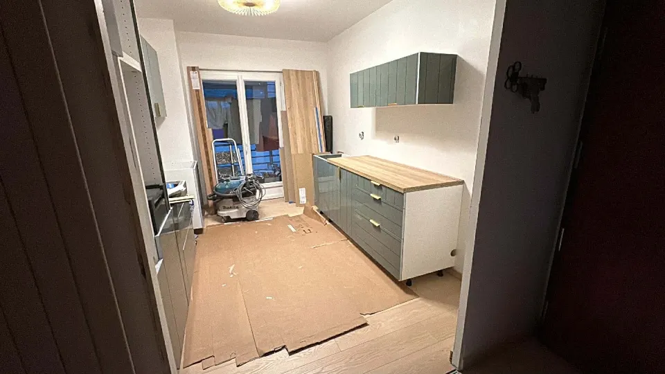 Pose des meubles bas verts et du plan de travail bois, sol protégé par du carton