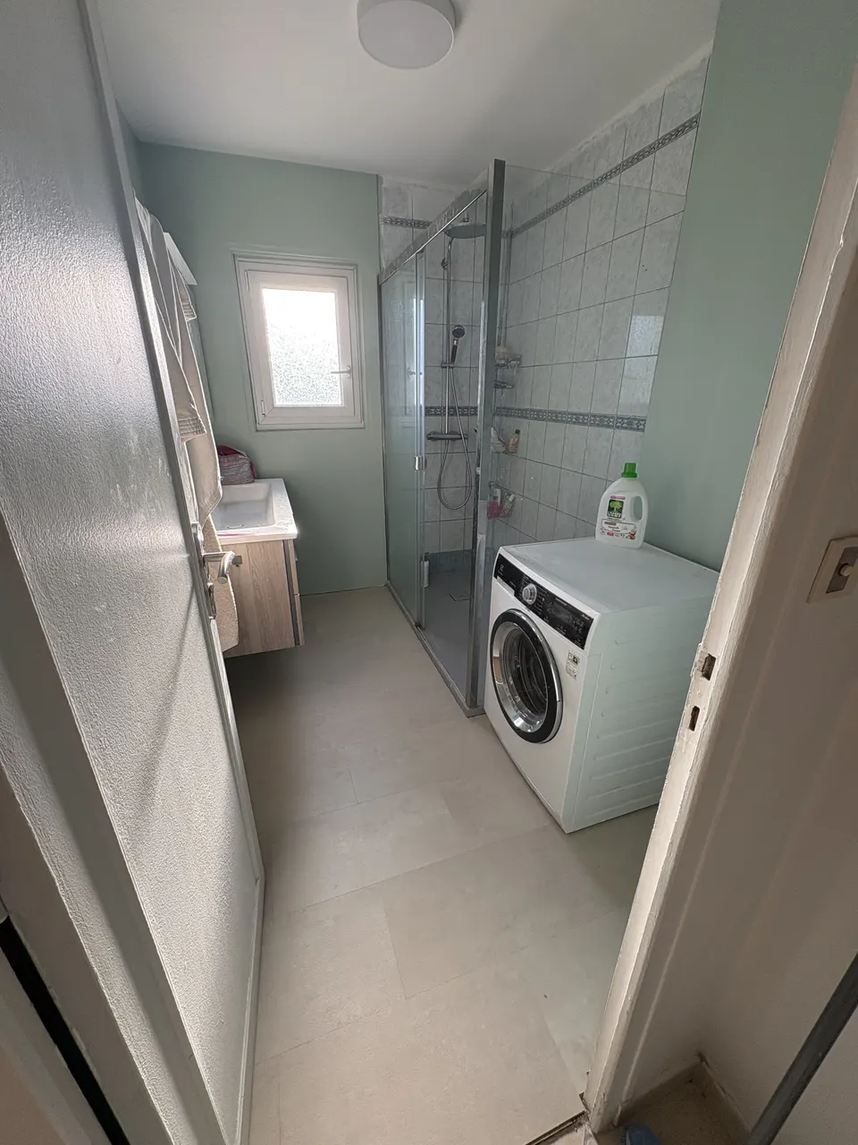 Salle de bain terminée : murs vert d'eau, sol clair, douche et lave-linge