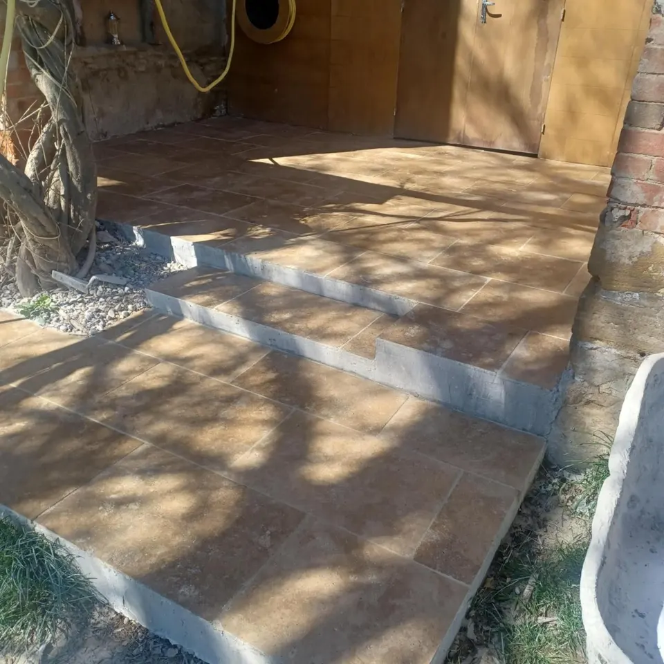 Terrasse terminée : dalles de travertin et marches posées au pied du mur en pierre.